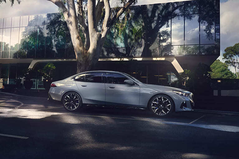 Weiße BMW i5 Limousine parkend an einer Straße vor einem Baum