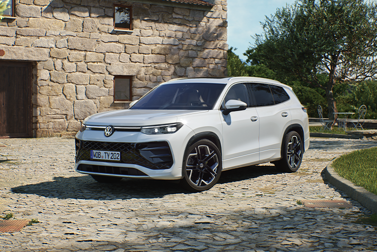 Weißer VW Tayron R-Line steht auf einem Kopfsteinpflaster vor einem Steinhaus. Modernes SUV mit sportlichem Design und schwarzen Felgen.